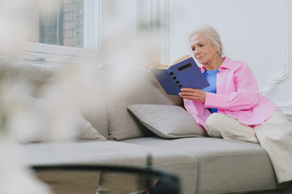 Person peacefully reading a book on a cozy sofa next to a window